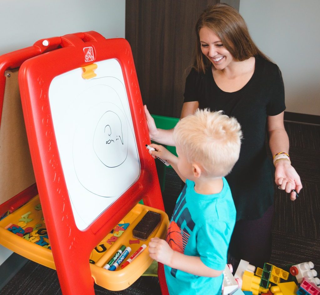 child writing on white board with therapist